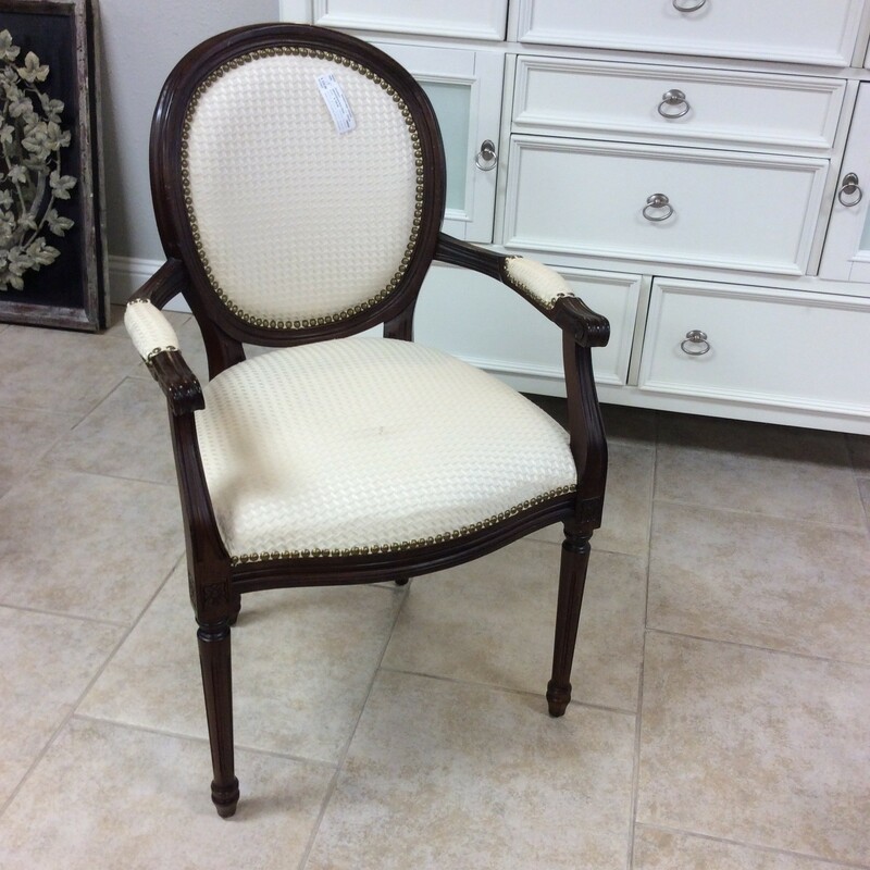 Pretty and petite. This armchair is traditional in style. It features a dark wood finish with carved details and has been upholstered in a cream colored fabric and includes a nailhead trim.