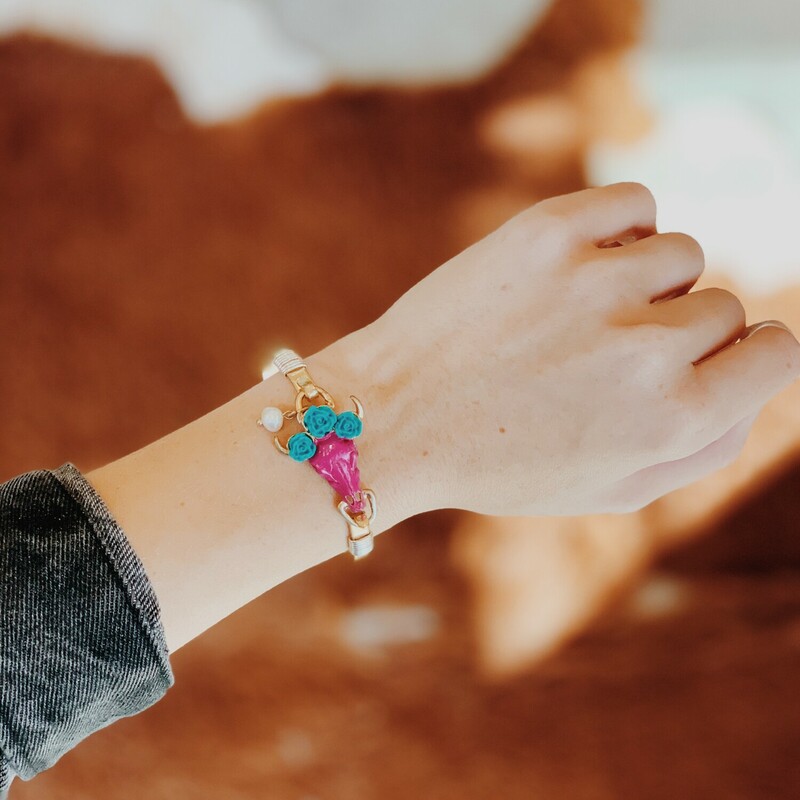 Adorable bracelet with a pink cow skull wearing three blue roses! The bangle is gold with silver accents.