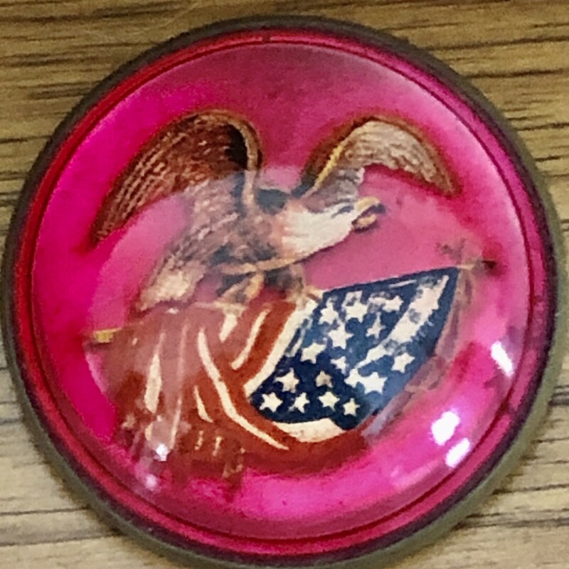 Victorian c.1890-1910 domed convex glass Bridle Rosette brooch style pin.
At 1-5/8 inches across, it features a die-cut  American Eagle on the flag.
The back of the rosette was designed to slide a horse bridle strap through.
