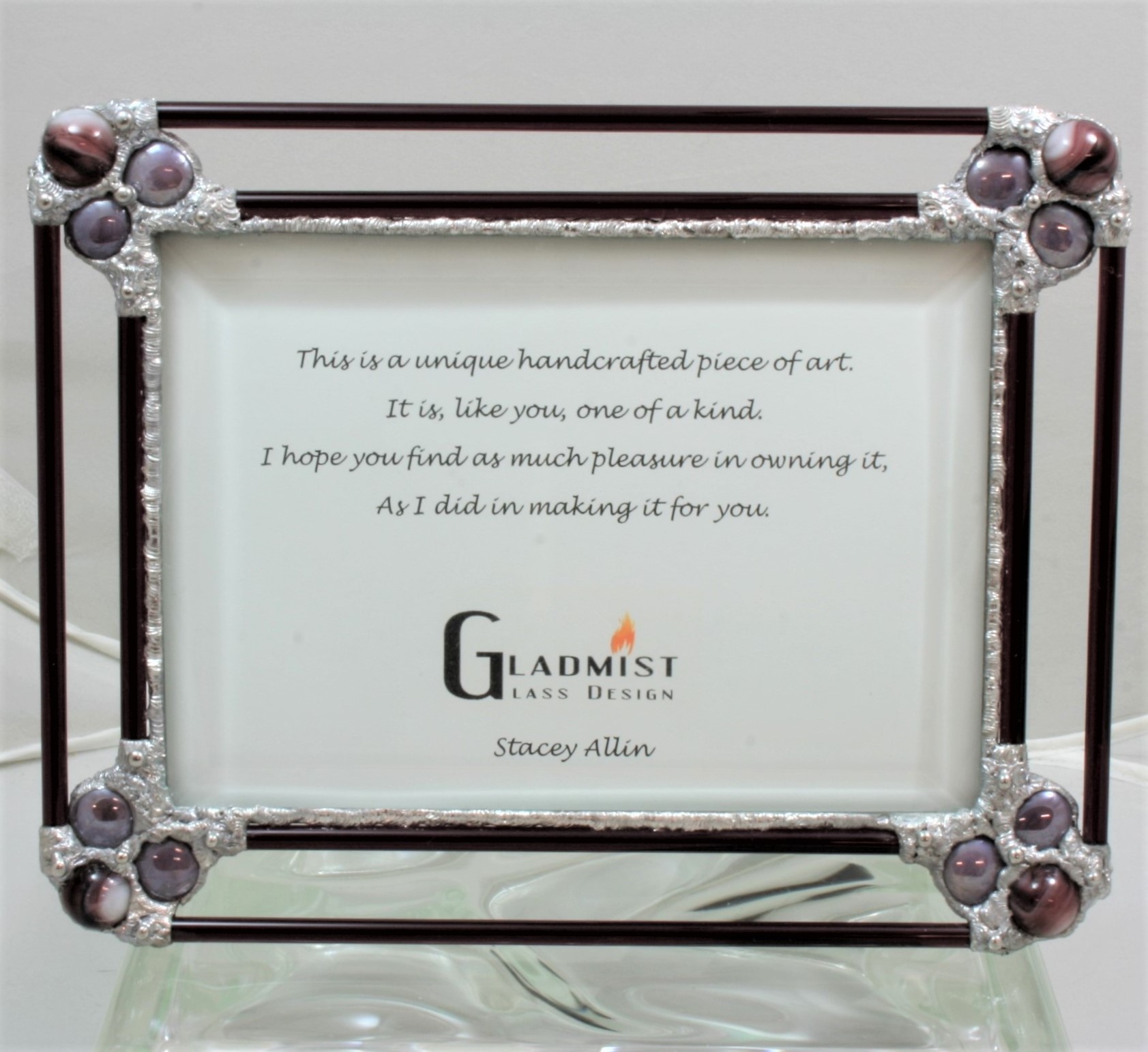 Purple glass frame by Gladmist Glass Design. Frame is made to fit a 5x7 picture under beveled glass. Can be displayed in horizontal or vertical position. Frame is made using glass rods, glass nuggets and glass marbles with decorative soldering.