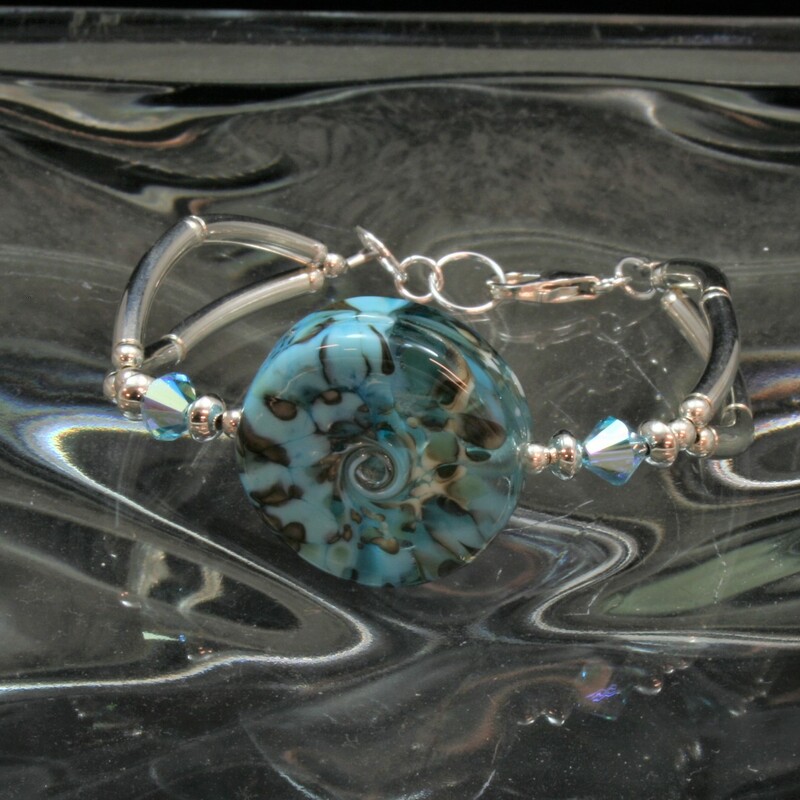 From the Seaside Cliffs collection of Gladmist Glass Design. Hand torched Lampwork glass beads combined with Swarovski crystals and Sterling Silver. Adjustable lobster clasp closure fits wrists 7 1/2 to 8 inches. Can be made to fit a larger wrist upon request.