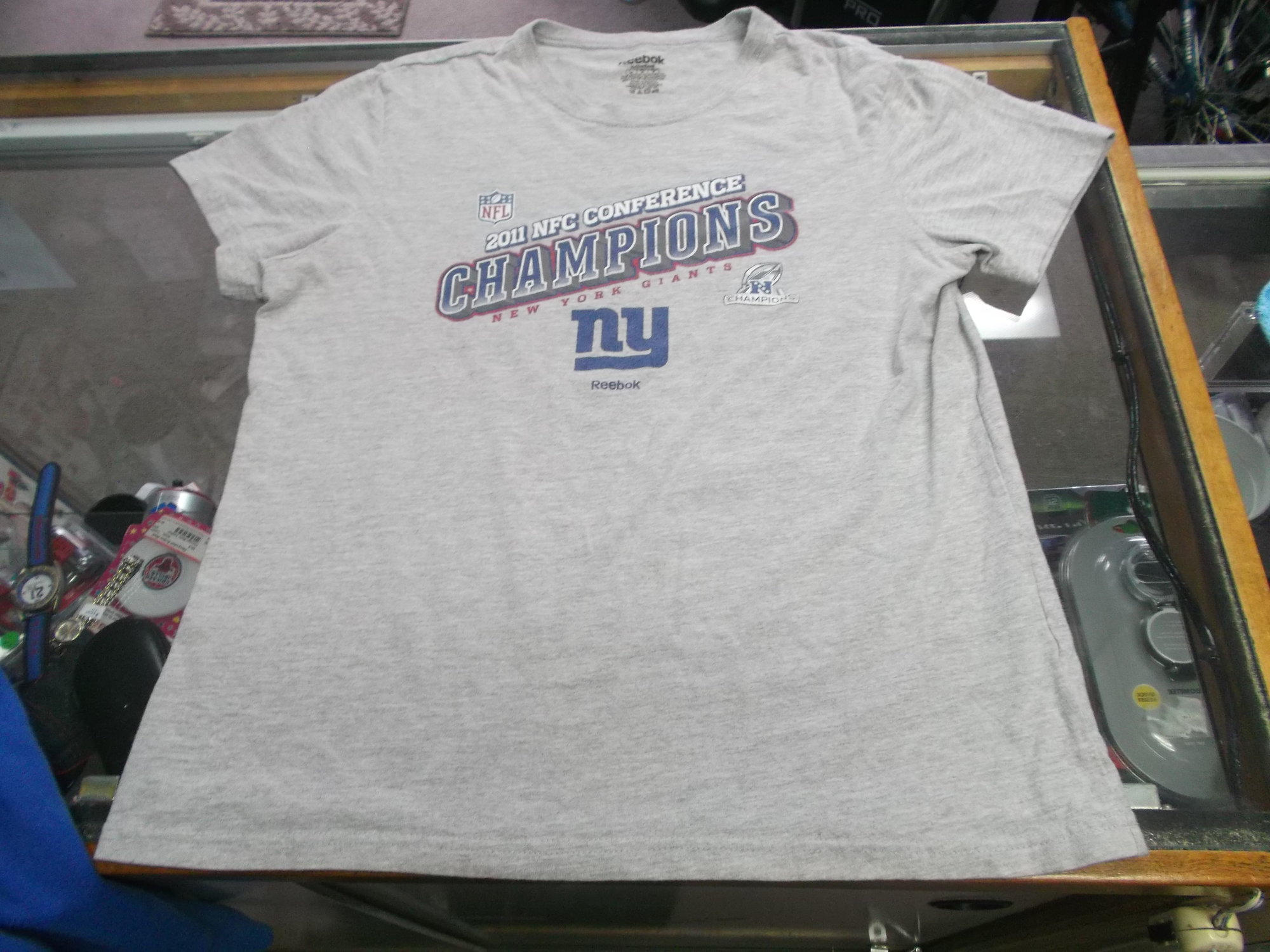 New York Giants 2011 Champions Women's Reebok Shirt Size Medium Gray #9476
Rating:   (see below) 4 - Fair Condition
Team: New York Giants
Event: 2011 NFC Champions 
Brand: Reebok
Size: Medium - Women's(Measured Flat: Across chest 19\"; Length 24\") 
Color: Gray
Style: short sleeve screen pressed Logo
Material: 93 Cotton 7 Polyester
Condition: - Fair Condition - wrinkled; Logo is faded and discolored; Significant pilling and fuzz; Material feels coarse; Definite signs of use; No stains rips or holes (Please use photos to see the condition details) 
Shipping cost: $3.37  
Item #: 9476