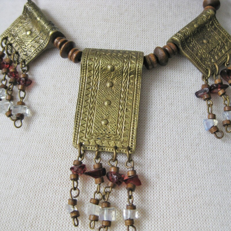 This tribal necklace is just a little longer than choker length.<br />
It has three brass tablets, each beautifully decorated with etched geometric designs.<br />
Each tablet has four dangles consisting of wood, white and red beads. I can't tell if the beads are actual stone chips, as they appear or plastic beads.<br />
The necklace is strung on a twisted cord.<br />
Length is 18in.<br />
Larger central tablet is 2in x 1in.<br />
<br />
Thanks for looking!<br />
#35432