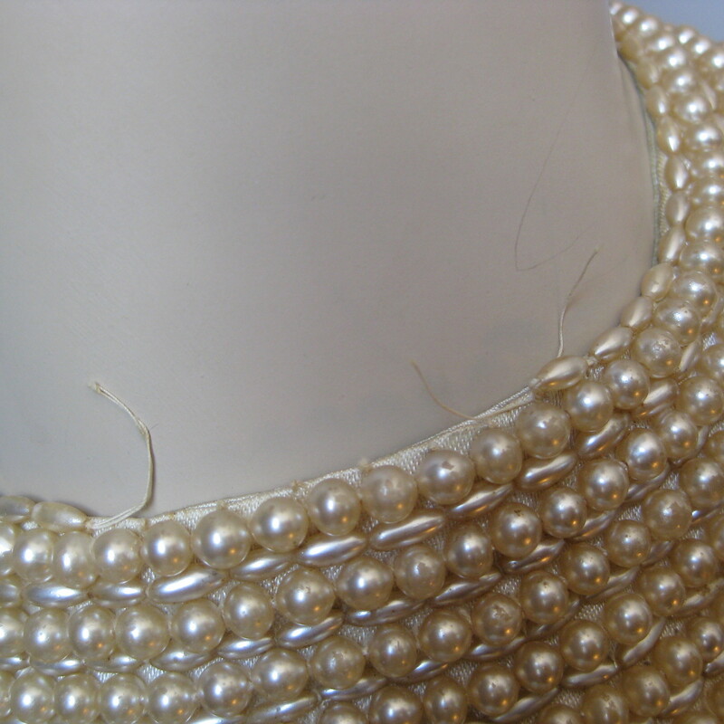 Vintage pearl collar from the 1940s or maybe 1950s.<br />
Wear over a plain top or as choker necklace.<br />
Faux pearls, satin backing.<br />
single hook and eye closure<br />
Great condition, the center of the top row of the longer narrow shaped pearls are missing but the pearls are sewn on in such a way that there won't be any further unraveling.  Some of the pearls have a bit of the finish rubbd off as well.<br />
Please see all the photos.<br />
Length: 15.75in<br />
<br />
Thanks for looking!<br />
#560