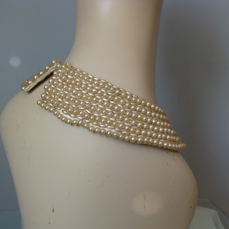 Vintage pearl collar from the 1940s or maybe 1950s.
Wear over a plain top or as choker necklace.
Faux pearls, satin backing.
single hook and eye closure
Great condition, the center of the top row of the longer narrow shaped pearls are missing but the pearls are sewn on in such a way that there won't be any further unraveling.  Some of the pearls have a bit of the finish rubbd off as well.
Please see all the photos.
Length: 15.75in

Thanks for looking!
#560