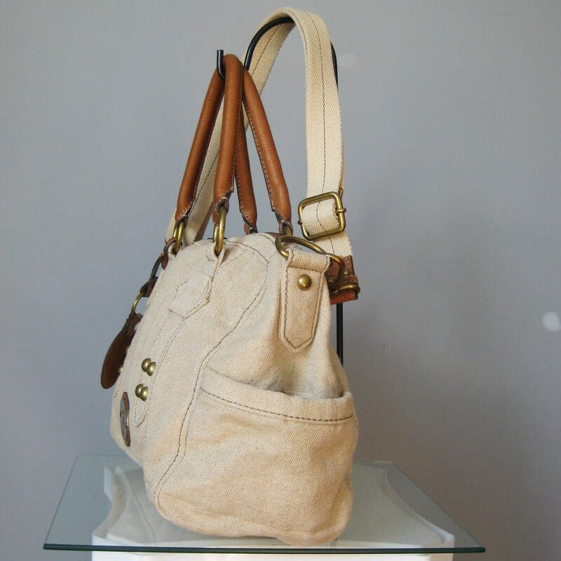 fabulous Fossil satchel in beige canvas with brown leather trim.<br />
Double leather handles and a detachable adjustible web shoulder strap<br />
Antique brass hardware<br />
Key bag charm and leather luggage tag<br />
two exterior slip pockets on the sides<br />
Chevron striped fabric lining<br />
<br />
Super clean inside and out<br />
tiny bit of use on the brass hardware medallion<br />
<br />
13in x 9in x 5in<br />
Handle drop: 6.25in<br />
Strap drop at max: 24.5in<br />
<br />
Thanks for looking!<br />
#18049<br />
<br />
Please see my eBay store for other terrific Fossil and other bags