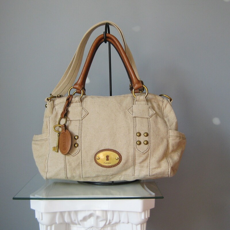 fabulous Fossil satchel in beige canvas with brown leather trim.<br />
Double leather handles and a detachable adjustible web shoulder strap<br />
Antique brass hardware<br />
Key bag charm and leather luggage tag<br />
two exterior slip pockets on the sides<br />
Chevron striped fabric lining<br />
<br />
Super clean inside and out<br />
tiny bit of use on the brass hardware medallion<br />
<br />
13in x 9in x 5in<br />
Handle drop: 6.25in<br />
Strap drop at max: 24.5in<br />
<br />
Thanks for looking!<br />
#18049<br />
<br />
Please see my eBay store for other terrific Fossil and other bags