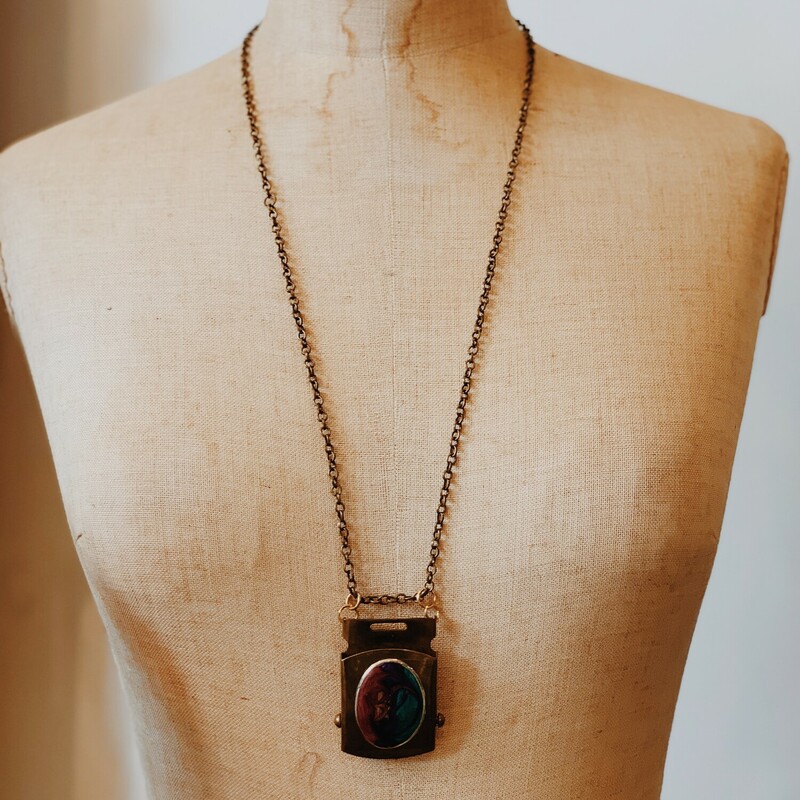 This unique necklace was handmade by one of our artists and features a brass buckle piece as its pendant! On the brass buckle is a swirl of colors. This necklace is on a 30 inch chain.