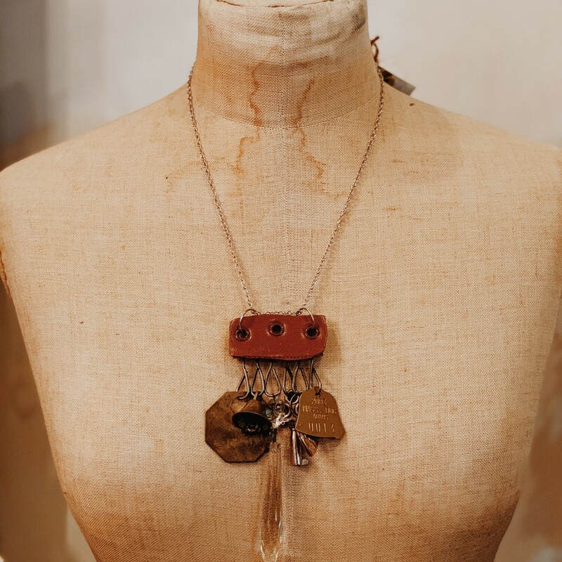 This one of a kind, handmade necklace is perfect for those who love unique! Hanging from leather is a golden hear locket, a brass bell, a crystal, and two brass tags. It is on a 20 inch chain.