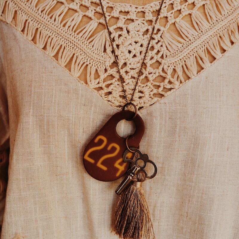 This one of a kind, handmade necklace has a cowtag with 224 on it, as well as a silver key and tassle. It hangs from a 26 inch chain.