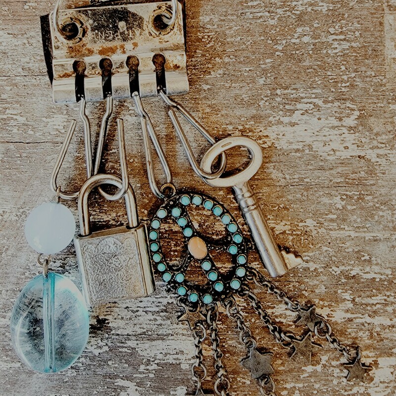 This one of a kind necklace was hand crafted! From a black leather strip hangs a silver key, a brass peace sign with blue and orange stones, a  silver padlock, and two blue beads. This all hangs on a 20 inch chain.