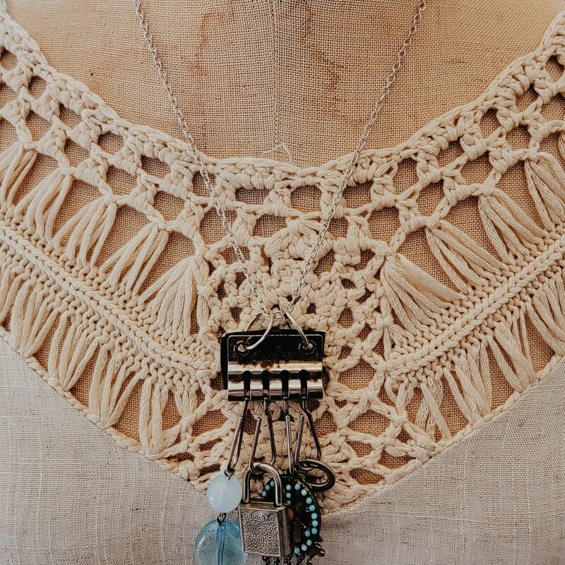 This one of a kind necklace was hand crafted! From a black leather strip hangs a silver key, a brass peace sign with blue and orange stones, a  silver padlock, and two blue beads. This all hangs on a 20 inch chain.