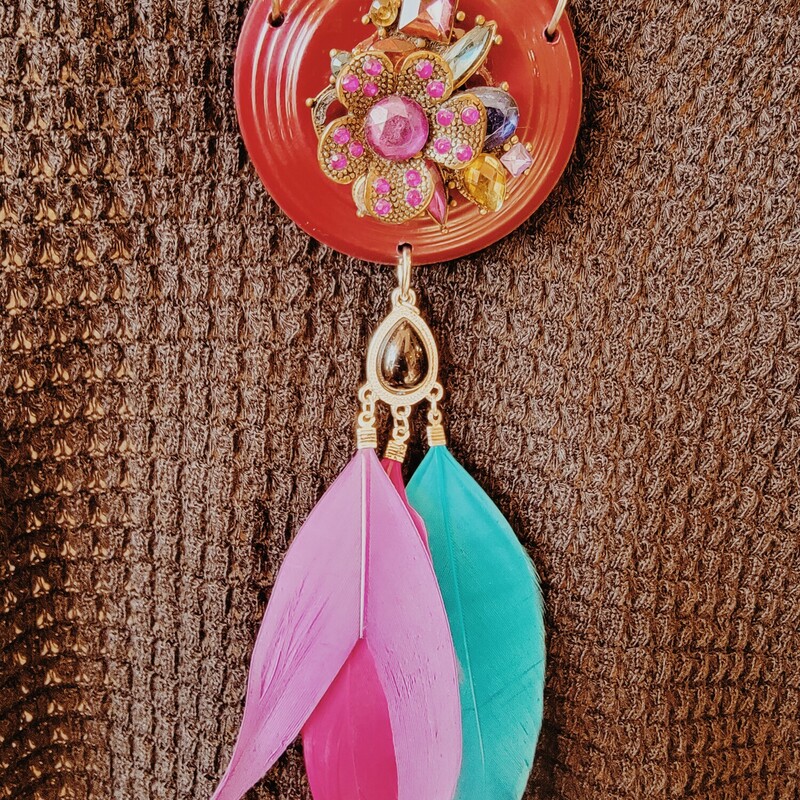 - Hand crafted necklace
- 32 Inch chain
- Escutcheon pendant with flower and gem center
- 4.5 Inch purple, blue, and pink feathers