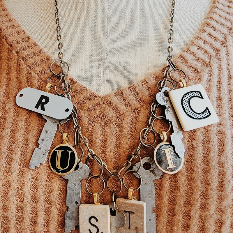 This one of a kind necklace spells out 'rustic' in game pieces and also has hanging keys. This necklace is on a 26 inch chain.