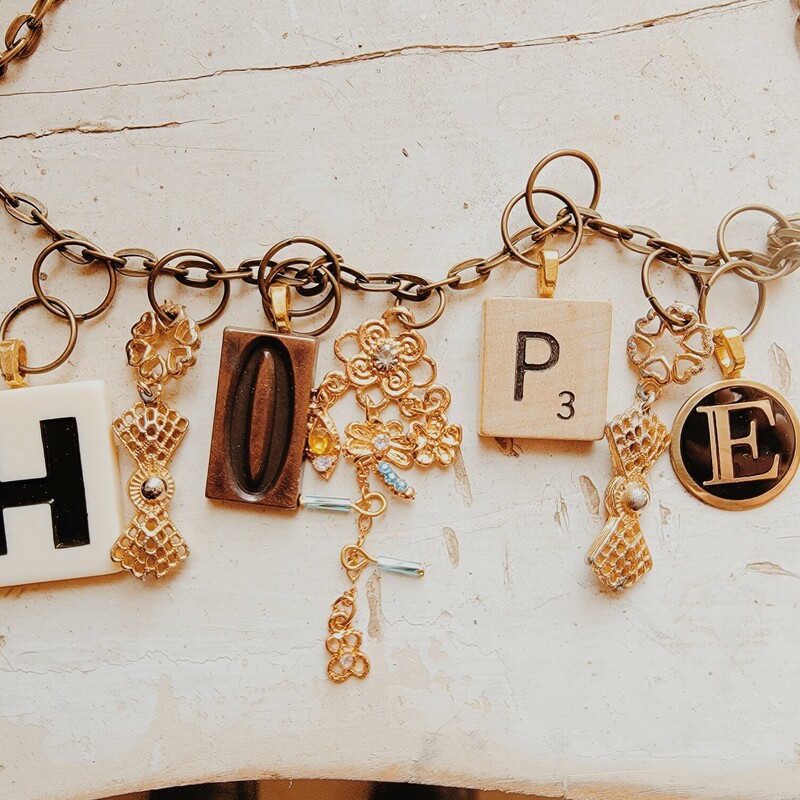 This beautiful necklace is on a 25 inch chain and spells out hope in game pieces! Also hanging from the chain are a variety of gold charms.