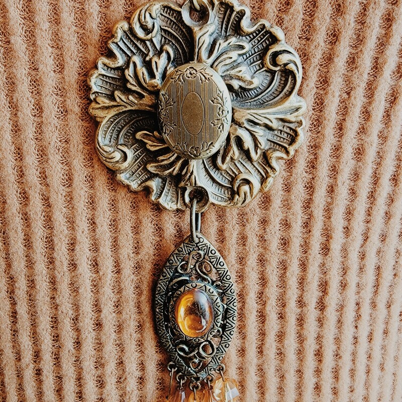- Hand crafted necklace<br />
- 30 inch chain<br />
- Brass flower pendant with locket center<br />
- Brass charm hanging from pendant with orange tone stones
