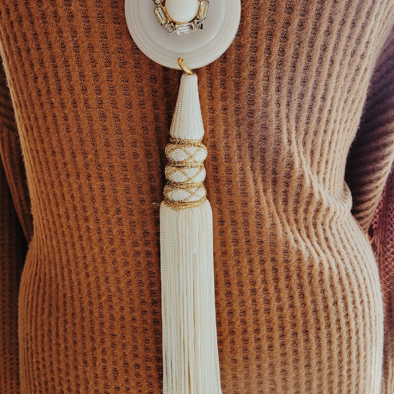 This beautiful, one of a kind necklace is on a 30 inch gold and pearl chain. It has an escutcheon as its pendant with a pearl like bead in the center. The tassel hanging from it is 8 inches long.