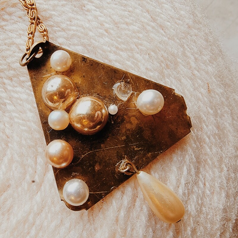 This handmade necklace has an antique brass triangle as its pendant with an assortment of faux pearls! It is on a 26 inch chain.
