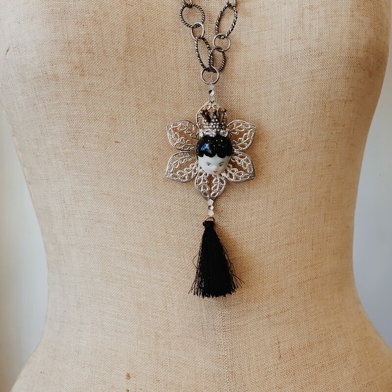 This necklace by Kelli Hawk Designs is truly one of a kind! It is on an excentric 30 inch chain with a 3 inch extender and has a silver flower pendant with a porcelain doll face attached and a black tassel hanging from it.