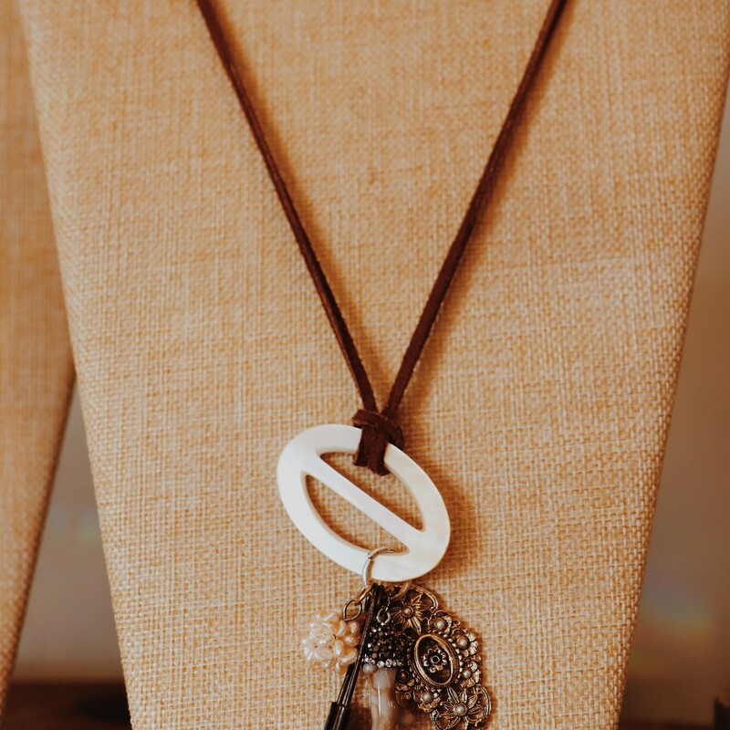 This beautiful handmade necklace by Kelli Hawk Designs has an iridescent buckle, a vintage brass charm, an antler, a vintage safety pin, and a cluster of pearls as the centerpieces. It hangs on a 20 inch leather cord.