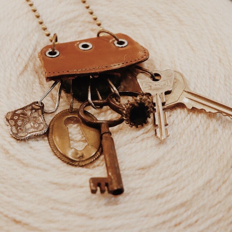 This unique necklace was hand crafted and has an assortment of charms hanging from leather that include keys, a ring, and a keyhole. It hangs on a 30 inch chain.