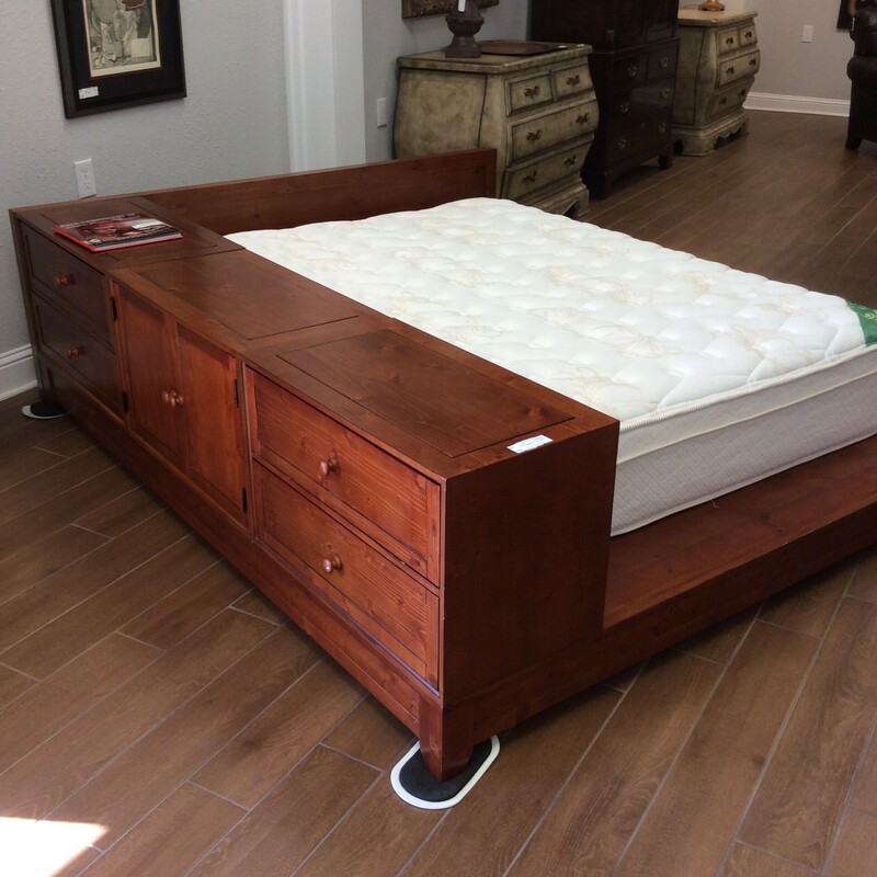 A very unique full size platform bed from Pottery Barn.
It has four drawers and two doors with shelves. The frame also has two lift out wood insets that expose holes for your cords to go through so you can set a tv on top of it or a lap top, lamp etc. The bed frame is a pine wood that is reddish in color. It also comes with the mattress!