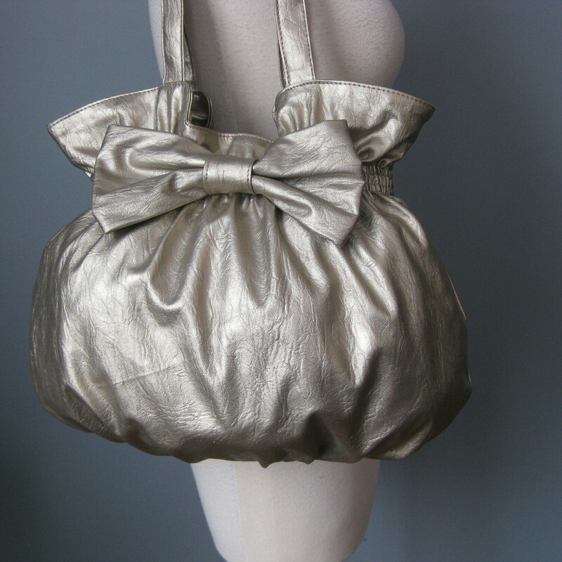 Shimmery Bow Shldr, Silver, Size: None<br />
Super cute and girly, this bag is a large shoulder bag in pale gold metallic vinyl.<br />
It has a pouch shape with a large bow on the front.<br />
Two nice wide straps, magnetic snap closure<br />
lined in light colored fabric with 1 zippered pockets and 2 slip pockets.<br />
<br />
No brand ID tag.<br />
Pristine!<br />
<br />
thanks for looking1<br />
#41885
