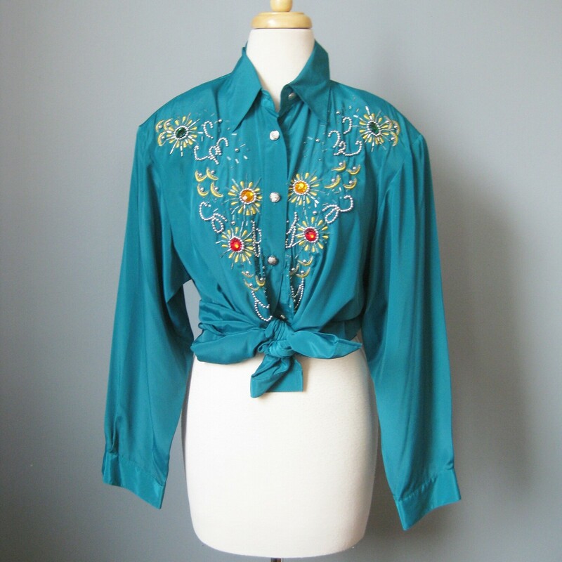 This long sleeved teal green shirt is lavishly bejeweled with large jewel tone stones  and gold beaded embroidery.

This piece was made in Hong Kong by Harbour Vue.   It's made of a slick matte polyester. The jewels are multi color plastic.  Good quality fabric in excellent condition.  Shoulder pads.

It is marked size 16, which I believe is pretty true to size today, but definitely use the measurements provided as your ultimate guide to fit.

These  are the flat measurements, please double where appropriate:
Shoulder to shoulder : 18
Armpit to Armpit: 21
Width at hem: 23
Underarm sleeve seam: 22
Length: 29 1/2

Thank you for looking.
#43094