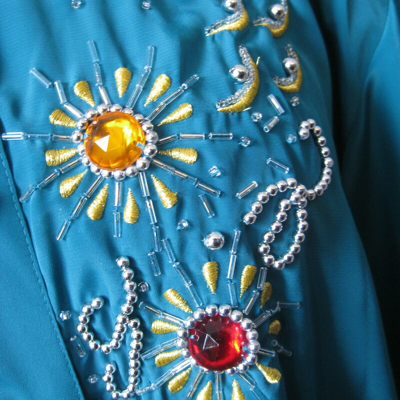 This long sleeved teal green shirt is lavishly bejeweled with large jewel tone stones  and gold beaded embroidery.<br />
<br />
This piece was made in Hong Kong by Harbour Vue.   It's made of a slick matte polyester. The jewels are multi color plastic.  Good quality fabric in excellent condition.  Shoulder pads.<br />
<br />
It is marked size 16, which I believe is pretty true to size today, but definitely use the measurements provided as your ultimate guide to fit.<br />
<br />
These  are the flat measurements, please double where appropriate:<br />
Shoulder to shoulder : 18<br />
Armpit to Armpit: 21<br />
Width at hem: 23<br />
Underarm sleeve seam: 22<br />
Length: 29 1/2<br />
<br />
Thank you for looking.<br />
#43094