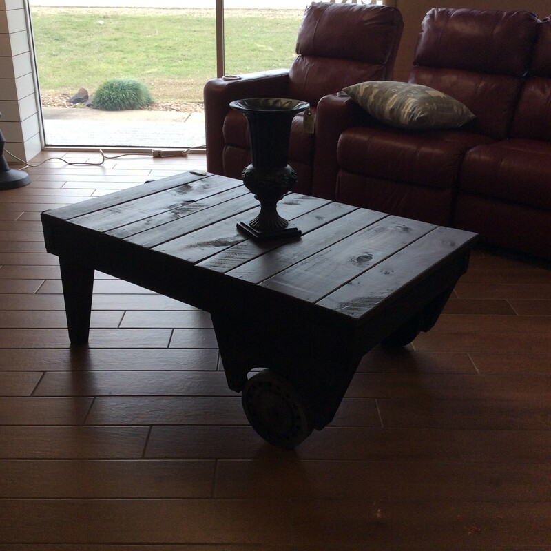 This custom-made coffee table is industrial in style. It features a dark wood finish and a wooden bar.