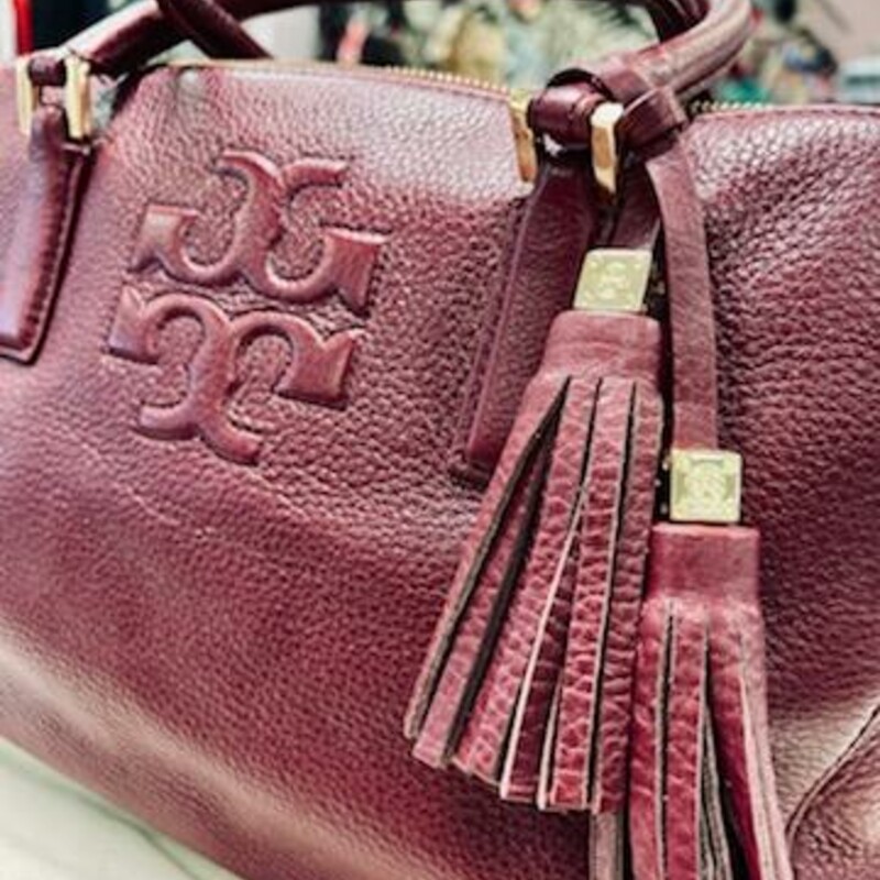 Tory Burch<br />
Thea Triple-Zip Satchel Bag rich Wine color<br />
<br />
Find a place for everything in Tory Burch's triple-compartment Thea satchel, a functional yet fun-to-wear design in enduring pebbled leather.<br />
Pebbled leather Tory Burch satchel with golden hardware.<br />
Rolled tote handles with rings, 5\" drop.<br />
Front and back zip-around compartments.<br />
Center zip-top compartment.<br />
Raised signature double-T logo at front.<br />
Hanging tassel detail with logo bead.<br />
Inside, one zip and two slip pockets; jacquard lining.<br />
9 1/2\"H x 13\"W x 6\"D.<br />
Bag weighs approx. 2.5.lbs.<br />
<br />
About Tory Burch: Tory Burch is a luxury lifestyle brand defined by classic American sportswear with an eclectic sensibility. It embodies the personal style and spirit of its CEO and designer, Tory Burch, who creates stylish and wearable clothing and accessories for women of all ages.<br />
Comes with the original dust cover.<br />
This bag is in excellet condition, gently used.
