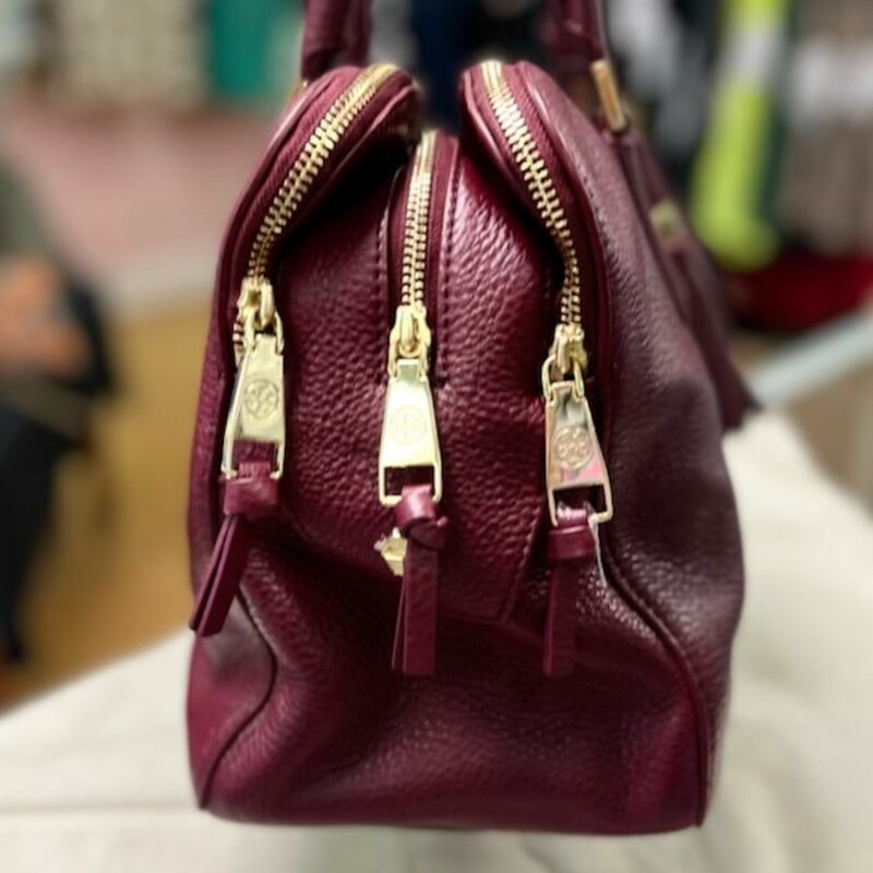 Tory Burch
Thea Triple-Zip Satchel Bag rich Wine color

Find a place for everything in Tory Burch's triple-compartment Thea satchel, a functional yet fun-to-wear design in enduring pebbled leather.
Pebbled leather Tory Burch satchel with golden hardware.
Rolled tote handles with rings, 5\" drop.
Front and back zip-around compartments.
Center zip-top compartment.
Raised signature double-T logo at front.
Hanging tassel detail with logo bead.
Inside, one zip and two slip pockets; jacquard lining.
9 1/2\"H x 13\"W x 6\"D.
Bag weighs approx. 2.5.lbs.

About Tory Burch: Tory Burch is a luxury lifestyle brand defined by classic American sportswear with an eclectic sensibility. It embodies the personal style and spirit of its CEO and designer, Tory Burch, who creates stylish and wearable clothing and accessories for women of all ages.
Comes with the original dust cover.
This bag is in excellet condition, gently used.