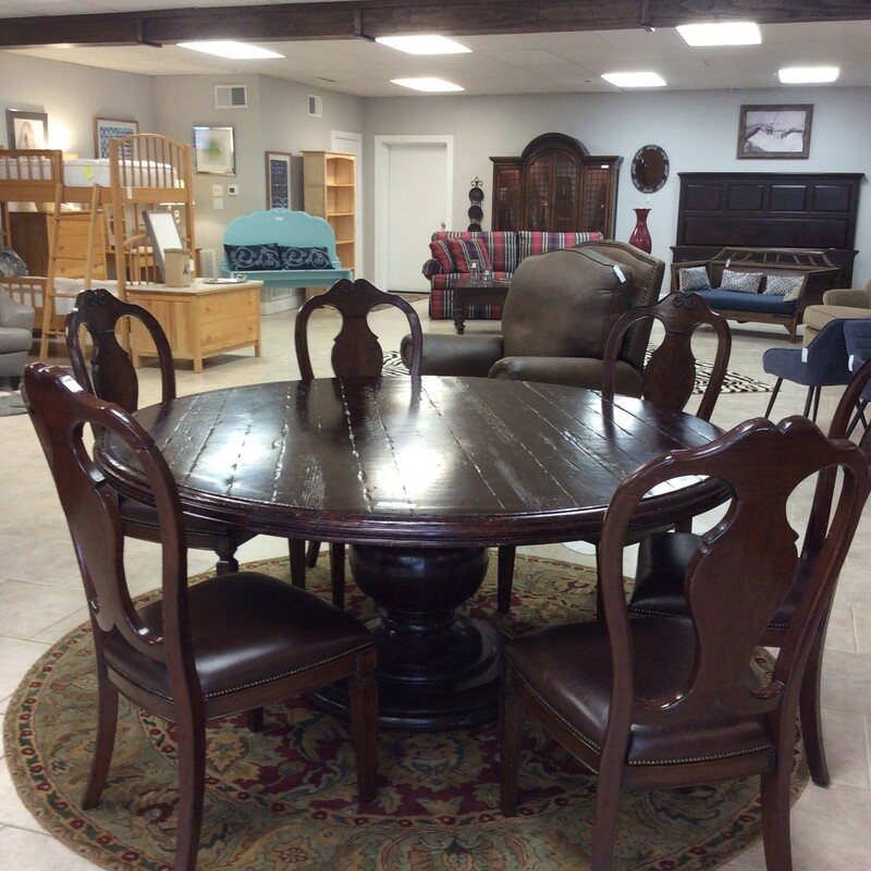 This diningroom set by Louis Shanks features a dark wood finish and 6 chairs.The table has a pedestal base and the chairs are upholstered in a brown leather with a nailhead trim.