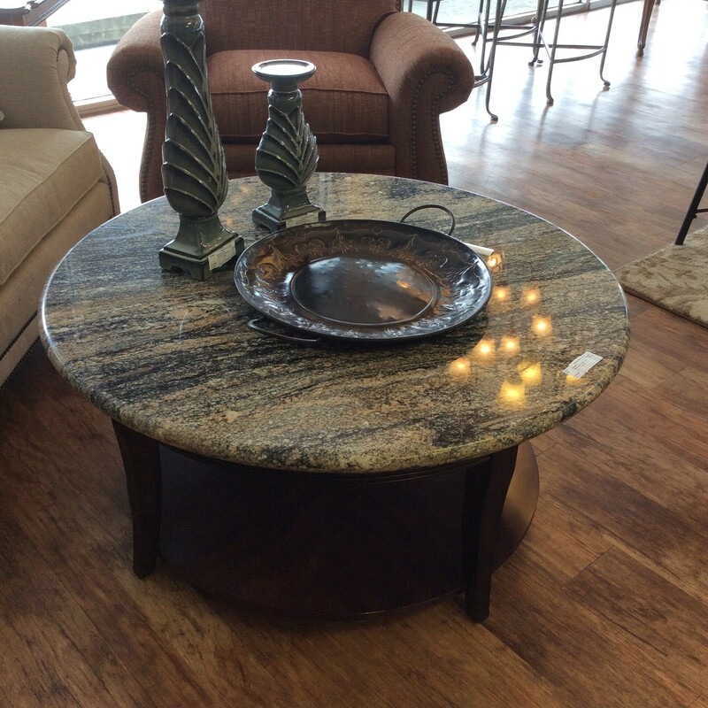 This round coffee table has a lower tier with a dark wood finish and the top is granite. It sits on casters that are beneath the table for easy portability.