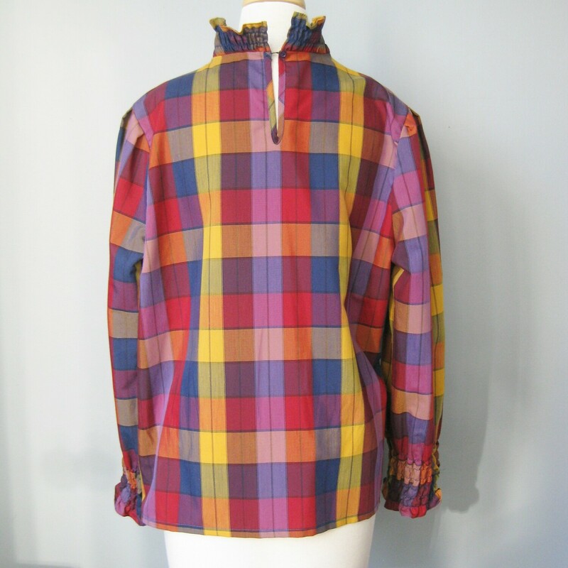 This plaid shirt from the 1970s was made by Essentially Separate<br />
The fit is relaxed and the medium scale plaid is a soothing mix of muted colors in navy and burgundy with a pop of yellow.<br />
the fabric is quite lightweight<br />
It has a high neck and both the neck and the ends of the long sleeves are elasticized for a ruffled effect.<br />
Elastic loop and button at the back of the neck.<br />
80% poly, 20% cotton<br />
<br />
Should fit a modern size large (marked size 18, but probably a bit small for a modern size 18)<br />
<br />
Here are the flat measurements of this shirt, please double where appropriate:<br />
Armpit to Armpit: 2: 2 1/2<br />
Width at hem: 24<br />
Length: 24<br />
shoulder to shoulder: 17 (no sh pads)<br />
nderarm sleeve seam: 17.25<br />
Length: 22 1/2<br />
Perfect condition.<br />
<br />
Thanks for looking.<br />
#40995