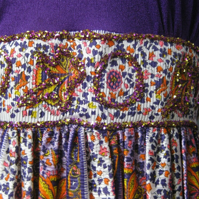 I believe this 1970s maxi dress was handmade.  It's quite special with gorgoues color, high ruffled neck, long sleeves and a sparlky sequined treatment at the waist.  These kinds of dresses lent a kind of boho glam to suburban patio entertaining.<br />
<br />
Synthetic knit fabric , probably nylon, with a little bit of stretch in the bodice.The fluid skirt has a vertically oriented floral strip pattern.<br />
<br />
The bodice is lined and there are color changes on that lining as shown.  A few minor picks on the bodice<br />
<br />
Center back zipper<br />
Should fit a modern size small to maybe medium, please use measurements provided to be sure.<br />
Flat measurements:<br />
Shoulder to shoulder 16.25<br />
Armpit to Armpit: 14.35<br />
Waist: 14<br />
Hip: up to 24<br />
Length :  56<br />
underarm sleeve seam: 16.5<br />
<br />
Thank you for looking!<br />
#38663