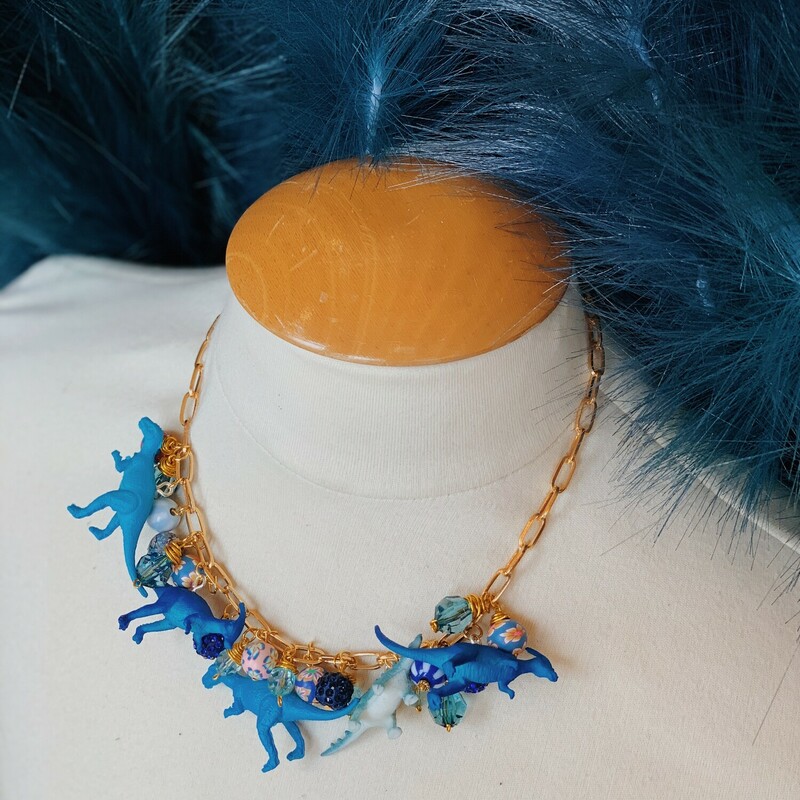 This one of a kind piece by Kelli Hawk Designs is on an 18 inch chain with a 2.5 inch extender. This gorgeous necklace is made of blue dinos and a variation of blue beads, all on a gold link chain! You can guarentee you are wearing one of a kind bling with this beauty!