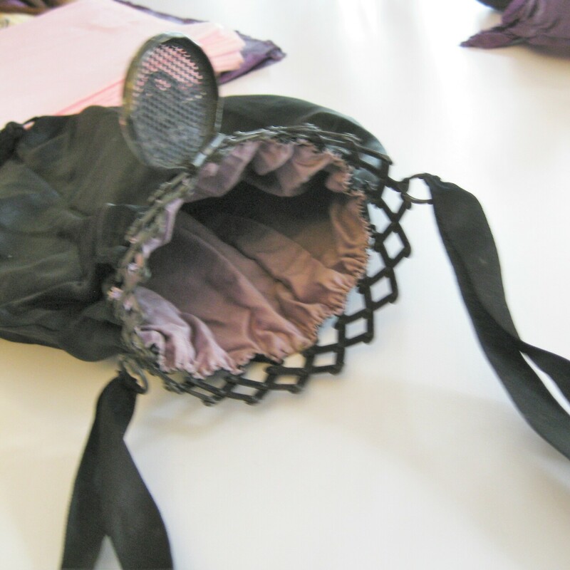 Very old silk purse, probably used as part of a Victorian or Edwardian mourning ensemble.<br />
This back is black with black satin ribbons and a metal expanding frame.<br />
The frame is topped with an open work metal cap with rhinestones.<br />
It has a dangling tassel at the bottom.<br />
The frame opens to reveal a dark lavender silk lining.<br />
Handmade.<br />
<br />
Amazing condition! no flaws<br />
<br />
10 wide at its widest point<br />
13 long/tall<br />
8 long<br />
12 around<br />
<br />
thanks for looking!<br />
#47337