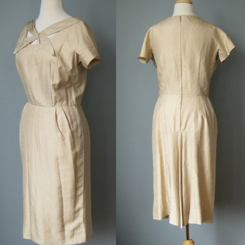 Very Smart, this slim fitting beige dress has a complex open neckline and a little flare of a train built into the back.<br />
<br />
This dress is made of slubby silk or faux silk shantung, in great condition. It is unlined and has a metal zipper in the center back. No labels. The sleeves are cut on short sleeves.<br />
<br />
excellent condition but with a few spots as shown in the photos, mostly in the back.<br />
<br />
Here are the flat measurements, please double where appropriate:<br />
<br />
Armpit to Armpit:  18.5<br />
Waist: 14 1/2<br />
Hips: 19 1/4<br />
Overall length: 41<br />
<br />
Thanks for looking<br />
#42825