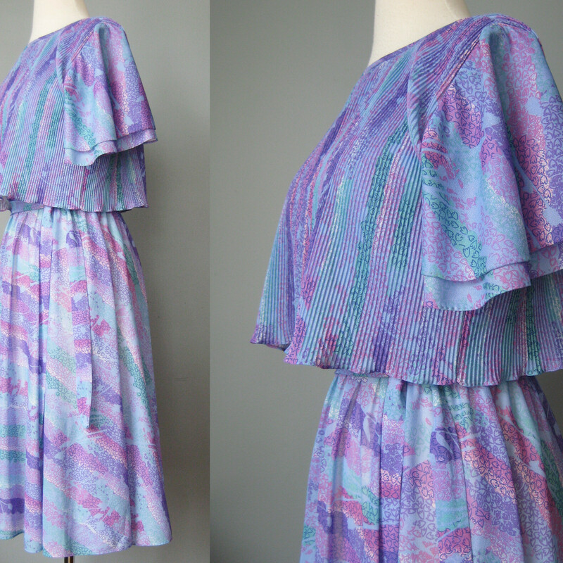 Vtg 70s Floral, Lilac, Size: Small<br />
Sweet below the knee dress in a very lightweight polyester.<br />
Abstract print in purples and blues.<br />
The dress has an elastic waist and a micro pleated capelet.<br />
Flutter sleeves and matching sash<br />
The skirt is sheer so you will need a half slip with it.<br />
No labels but I believe this is from the late 70s, on the cusp of disco fever and it reminds me of the dresses worn by the heroine of Saturday Night Fever.<br />
<br />
Here are the flat measurements, please double where appropriate:<br />
Shoulder to shoulder: 15.5<br />
Armpit to Armpit: 20<br />
Waist:  13 stretches comfortably to 16<br />
Hip: free<br />
length: 39<br />
<br />
Thanks for looking!<br />
#41301