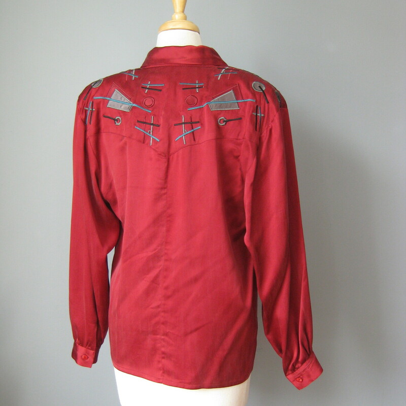 Gary Fabrikant washed silk blouse in deep almost burgundy red.<br />
Bit shoulder pads support a decorative shoulder and back yoke, embroidered and appliqued with gray, teal and red geometric designs.<br />
Asymmetrically set buttons pair off down the front<br />
Button Cuff Sleeves.<br />
Nicely made with an interior button to keep that neckline under control.<br />
Perfect condition.<br />
flat measurements:<br />
shoulder to shoulder: 20<br />
armpit to armpit: 20<br />
length: 25.5<br />
Underarm sleeve seam length: 18<br />
Width at hem:  19.5<br />
<br />
thanks for looking!<br />
#45422