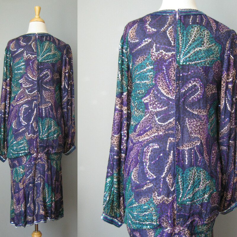This spectacular sequined silk cocktail dress from the 1980s is perfect for festive evening occasions or a 1920s themed formal party.   The dress is silk and in peacock colors of blue green and purple.  Beaded and embroidered with an abstract fireworks designs.<br />
<br />
The dress has a dropped blouson waist and a short pleated skirt<br />
Long sleeves and center back zipper.<br />
<br />
100% silk by Judith Ann creations. Made in India<br />
<br />
the bad news is that the lining at one shoulder is damaged and weak overall.  It could use a new lining.<br />
It can be worn as is if you are super careful putting it on and taking it off.  I've priced it accordingly!<br />
<br />
Marked size M but better for a small.<br />
Here are the flat measurements, please double where appropriate:<br />
Shoulder to shoulder: 15.5<br />
Armpit to Armpit: 19.25<br />
Waist: 20<br />
Hips: 19<br />
Length from back of neck to hem: 42<br />
<br />
<br />
Thank you for looking.<br />
#46129