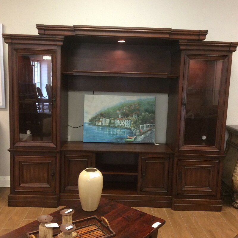 This is a large adjustable, dark stained Entertainment Center. This entertainment center has 2 glass cabinets with 2 adjustable shelfs in each cabinet, 4 wood door cabinets with 1 shelf in each, 2 shelfs between cabinets and 3 overhead lights.
