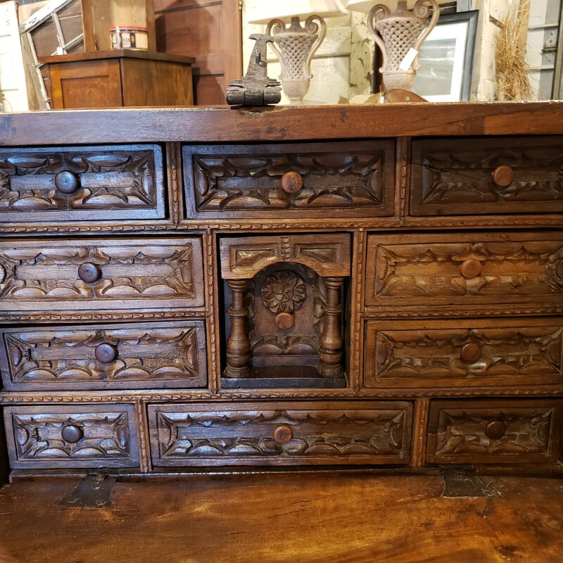 Antique Chest/Writing Desk. One of a kind carved wood chest with iron hardware. Worm eaten wood drawers. Center drawer has a hidden compartment. In good condtion for its age, with some wear. The latch does not close, but the lock does work. Size: 29.5x12.5x18.5