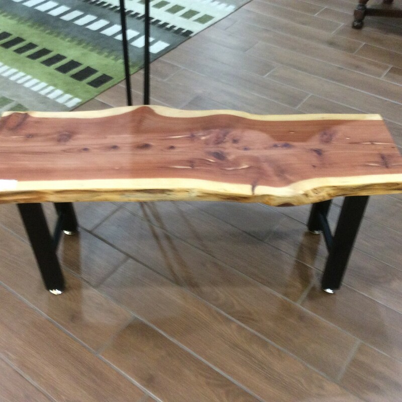 This cedar wood bench has a live edge and a black metal base.