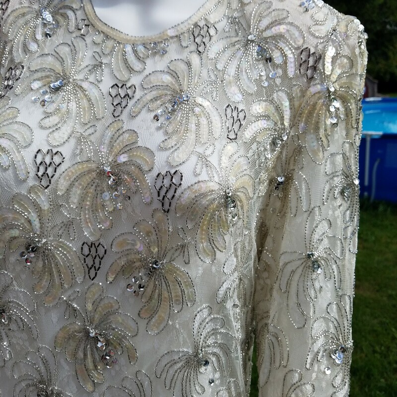 VINTAGE JUDITH ANN CREATIONS<br />
SILVER BEADED GOWN<br />
SIZED L<br />
THIS DRESS IS AMAZING<br />
MAYBE WORN TWICE<br />
RARE FIND<br />
Intricate, detailed beading and floral sequins adorn the garment. Full-length sleeves. Drop waist, with 'zig-zag' bead design leading to a fuller skirt with scalloped hem. This garment is completely sheer, you may wish to wear with a slip. Measurements: Original tag adv. size L. The material is very stretchy, and is not designed to be worn tight-fitted. Bust: 44 Waist: 40 Hips 44 Length: 55 Excellent, vintage condition. May be some missing beads