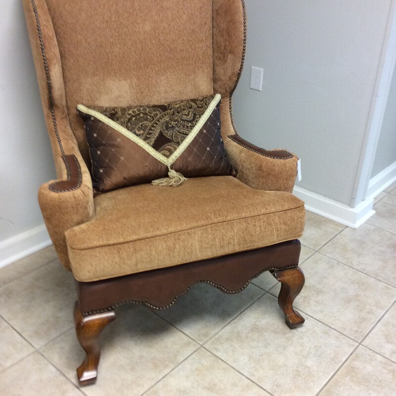 This large wingback chair has tan upholstery with leather accents and nailhead trim.