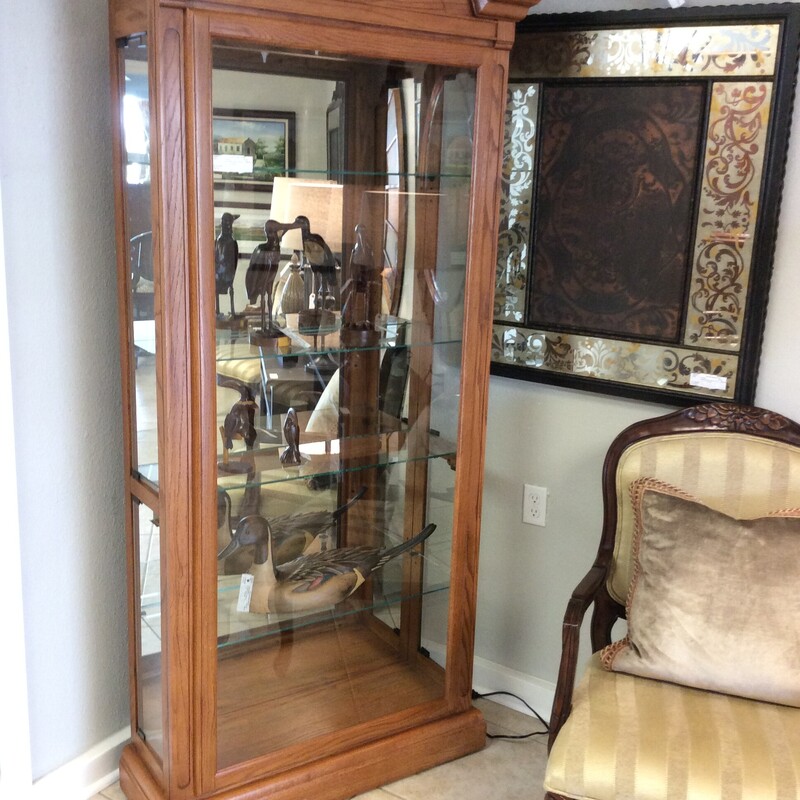 This curio cabinet has a  medium oak finish with 4 glass shelves. There is a carved pediment, bulit in light, and side panel glass doors.