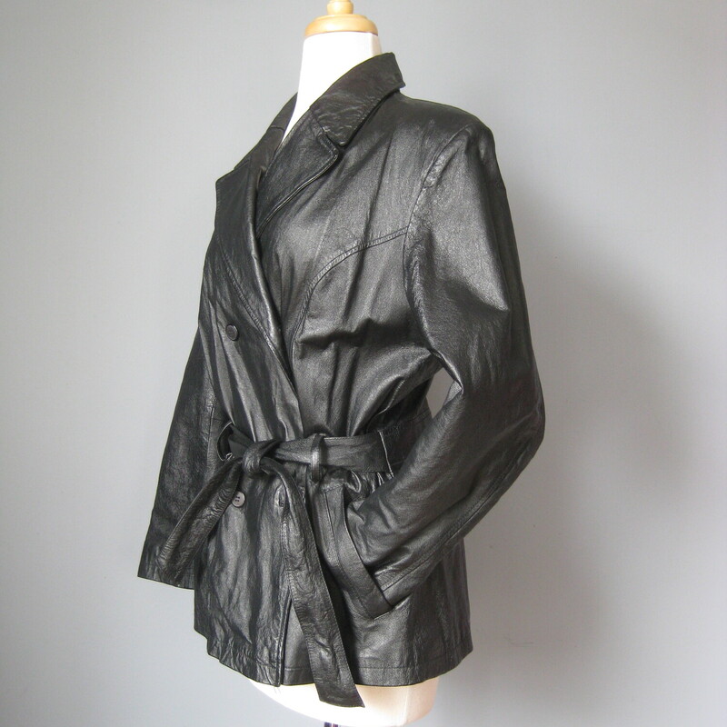 This simple hip length double breasted black leather trench coat has an attached belt, button closures<br />
It has pockets, a cool notched lapel<br />
<br />
Fully lined with a medium weight quilted fabric for a bit of warmth. (no batting)<br />
It has pretty big shoulder pads built in under the lining.<br />
<br />
Excellent condition!<br />
<br />
Here are the flat measurements:<br />
<br />
Armpit to armpit: 23<br />
Width at hem: 22<br />
Length: 28<br />
underarm sleeve seam: 15.5<br />
<br />
Thanks for looking!<br />
#54011