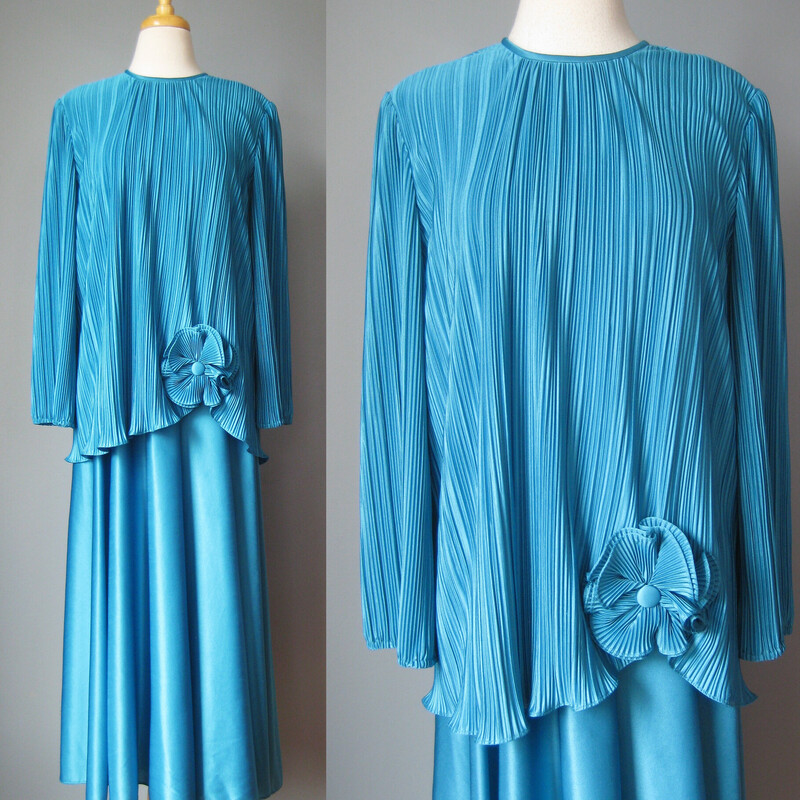 Vtg Mister Jay Gown, Blue, Size: XL

This fun dress looks like a two piece set but it is one piece
The bodice is micropleated and tunic length with long sleeves.  The bottom edge is free and is adorned with a large fabric flower.
The dress underneath is unlined, unpleated and has an elastic waist
Small shoulder pads, more to support the weight of the gown that to add to the silhouette.
the sleeve ends are gathered and elasticized.
somewhat stretchy polyester
by Mr. Jay

No size tags
flat measurements:
Shoulder to shoulder: 16
armpit to armpit: 23
waist: 13.5 stretches comfortably to 17
hip: free
length: 53
underarm sleeve seam length: 16.5


Thanks for looking!
#46136
